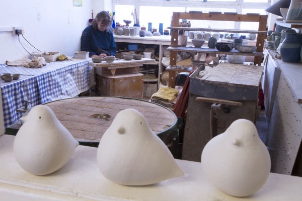 Jane working in her pottery studio with ceramic doves on a shelf in the foreground
